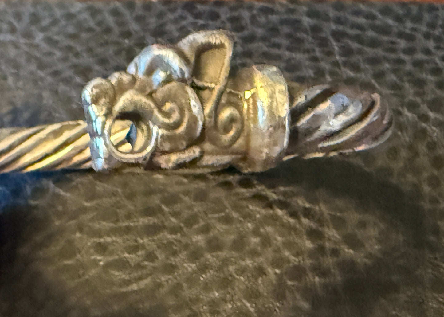 Silver bracelet with intricate design held by a hand on a textured surface