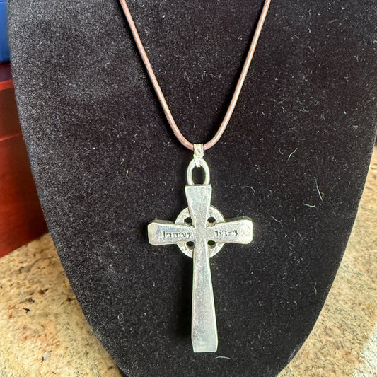Silver cross pendant on a brown leather necklace against a dark background