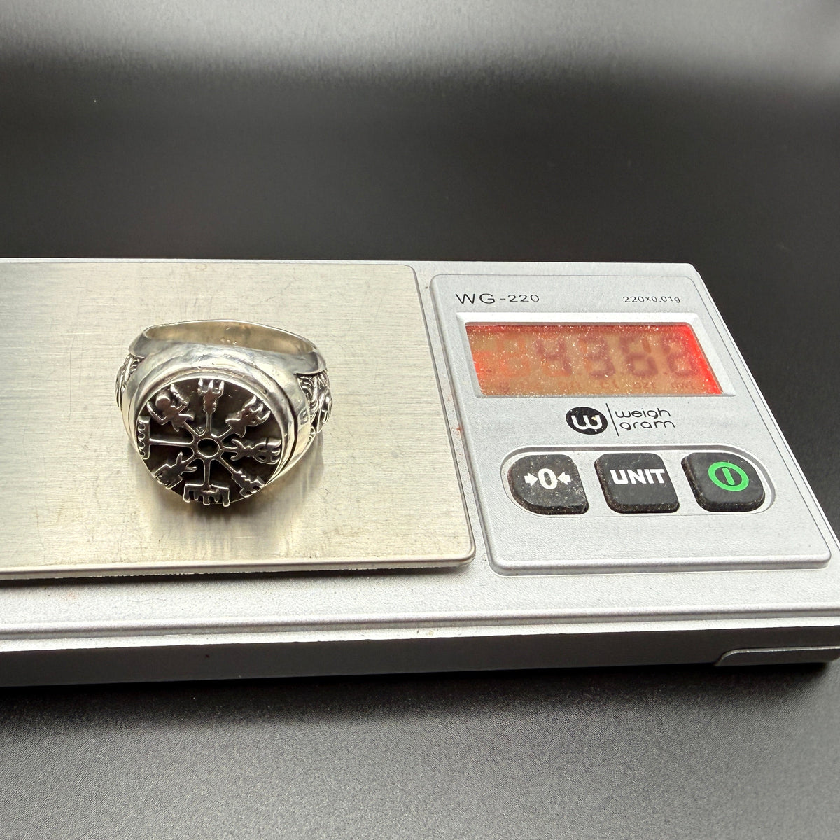 A sterling silver Viking-style ring with a raised compass motif and textured details on scale showing 43.86 gram weight