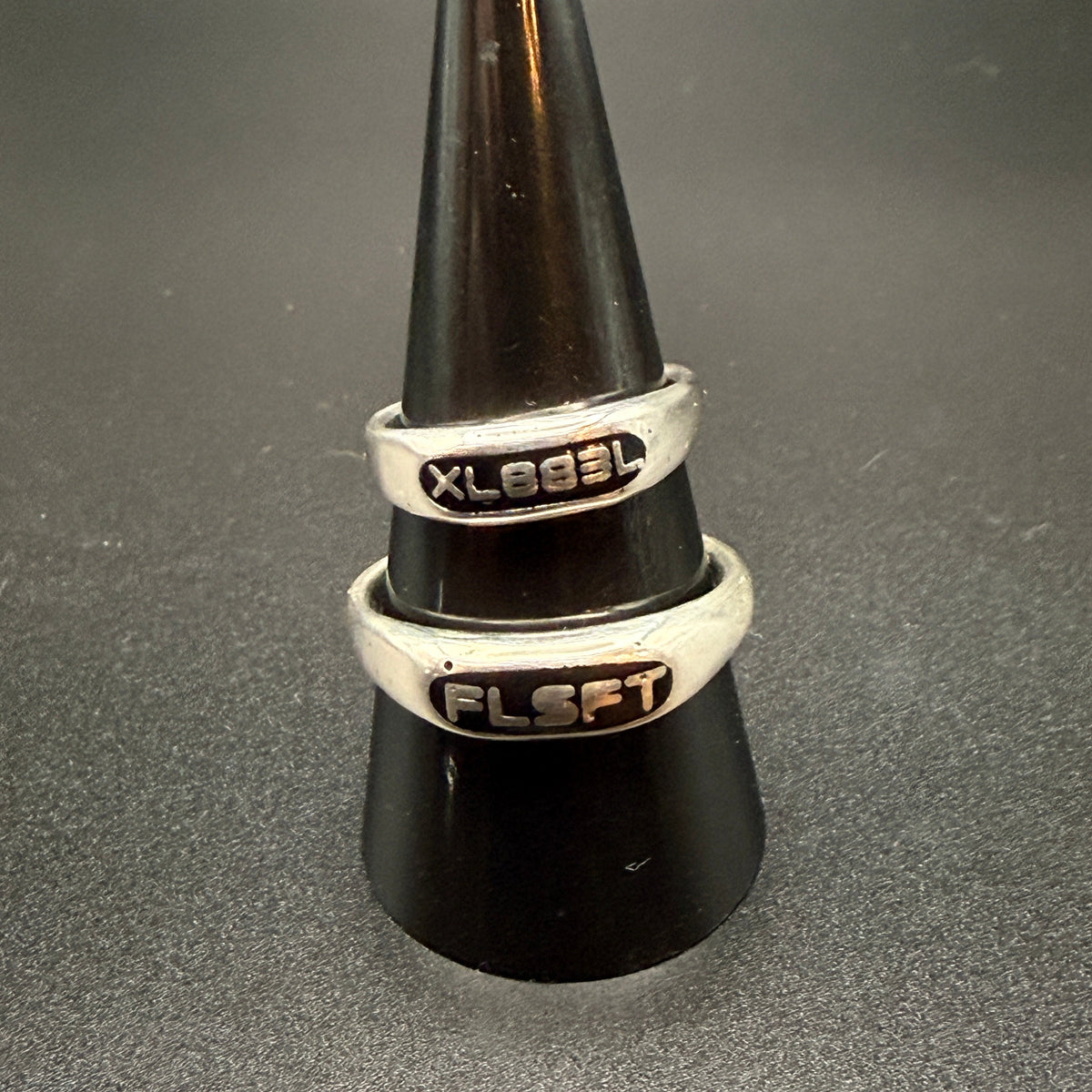 Two narrow sterling silver signet rings with custom embedded lettering reading "XL883L" and 'FLSFT'