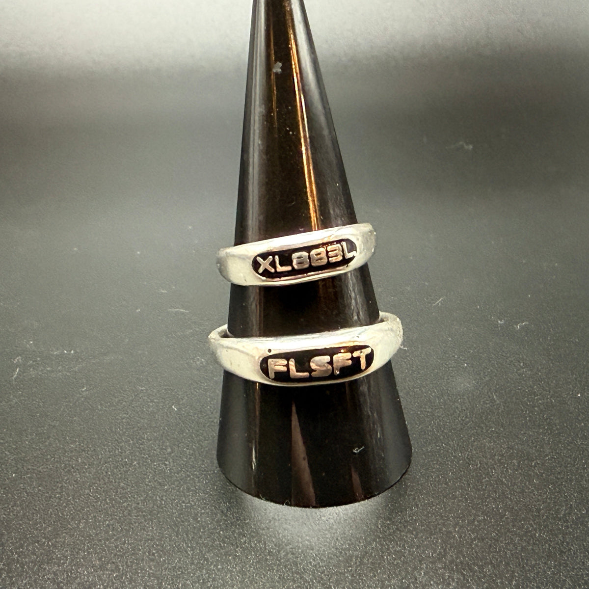 Two narrow sterling silver signet rings with custom embedded lettering reading "XL883L" and 'FLSFT'