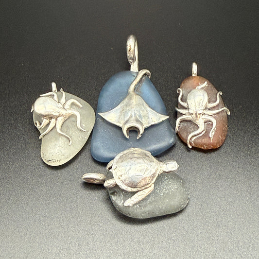 Collection of sterling silver sea creature charms affixed to real sea glass of varying colors.