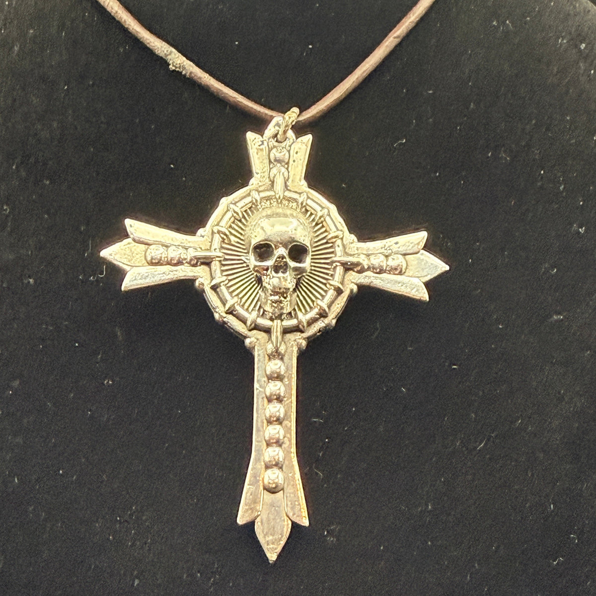 A gothic-style cross pendant necklace featuring a skull at the center and arrow details on the arms.