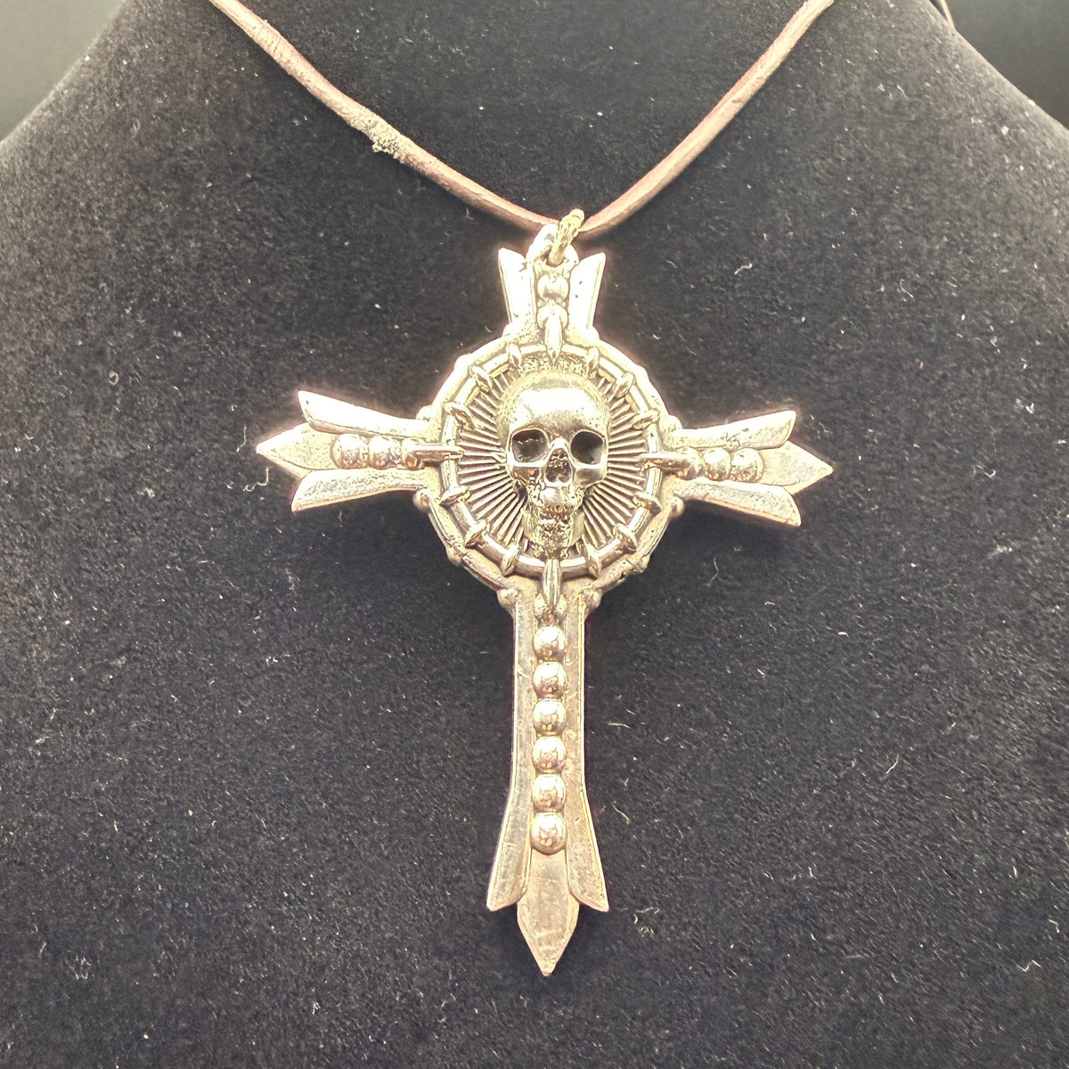 A gothic-style cross pendant necklace featuring a skull at the center and arrow details on the arms.