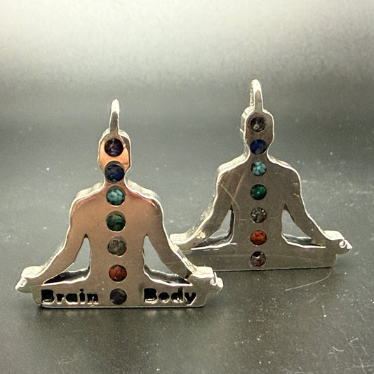 A pair of sterling silver chakra pendant shaped like meditating figures, featuring seven chakras colored with natural stone chips