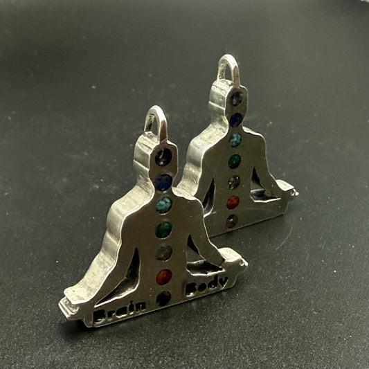 A pair of sterling silver chakra pendant shaped like meditating figures, featuring seven chakras colored with natural stone chips