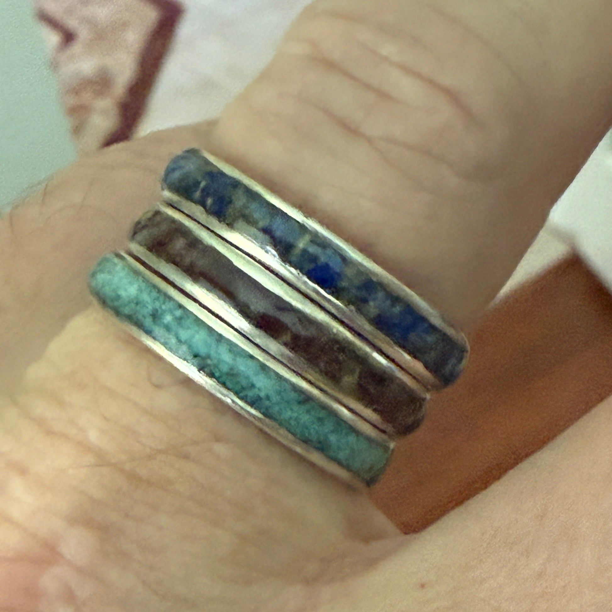 Close-up of a hand wearing a stack of colorful rings on a neutral background