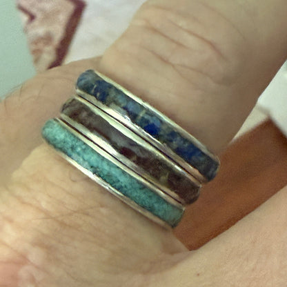 Close-up of a hand wearing a stack of colorful rings on a neutral background
