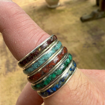 Multicolored gemstone ring on a finger with a blurred outdoor background
