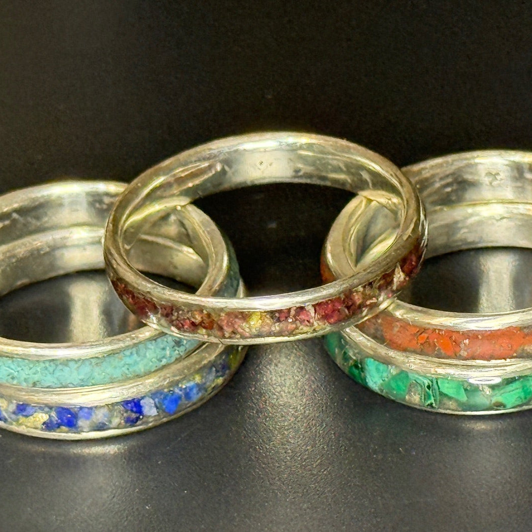 Five silver rings with colorful inlay on a black background
