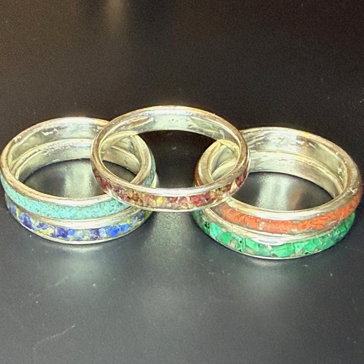 Five silver rings with colorful inlay on a black background