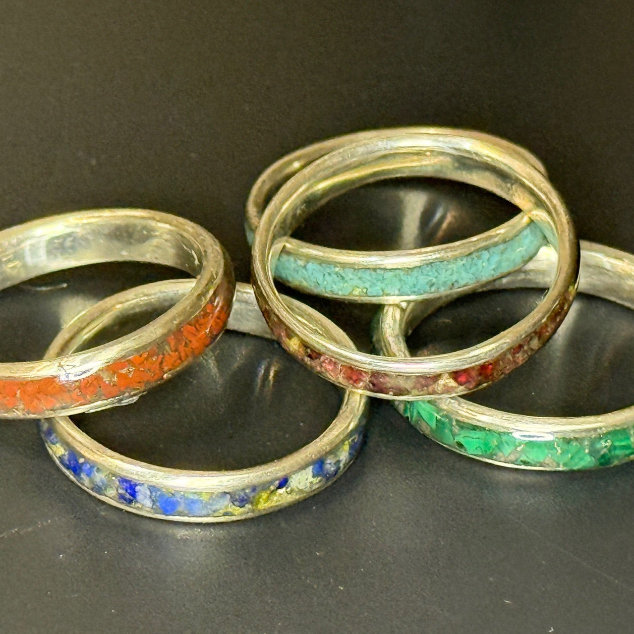 Five rings with colorful inlays on a dark surface